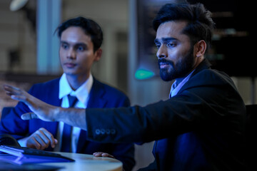 A diverse team of AI developers collaborates on a night coding session. A senior engineer oversees his team, intensely focused on debugging a complex machine learning project.