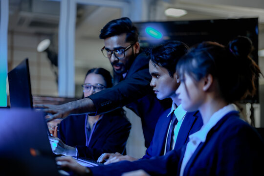 A diverse team of Asian and Indian AI developers collaborates on complex code. A senior engineer oversees his team, intensely focused on a machine learning project at night.