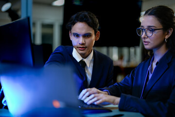 A diverse team of AI developers in a pair programming session. The female programmer and her male colleague collaborate, intensely focused on coding a complex new algorithm at night.