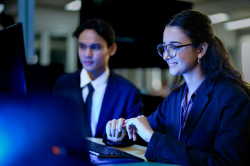 A diverse team of AI developers in a pair programming session. The female programmer and her male colleague collaborate, intensely focused on coding a complex new algorithm at night.