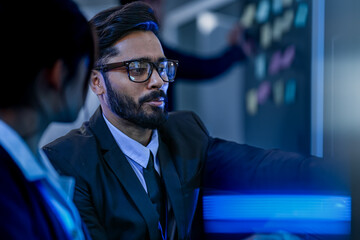 A diverse team of AI developers celebrates a successful breakthrough. A smiling senior engineer points to the screen, showing his colleague the positive results of their new algorithm.