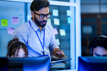 A diverse and inclusive team of software developers collaborates on a project. A female team lead discusses code with her colleagues, one of whom is in a wheelchair, in a modern office.