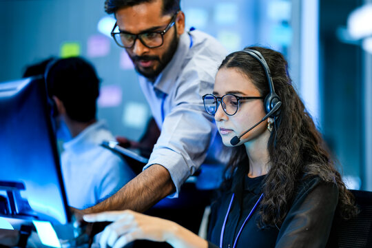A diverse team of technical support specialists works a late shift in a busy call center. Focused operators with headsets assist clients, providing all day customer service.