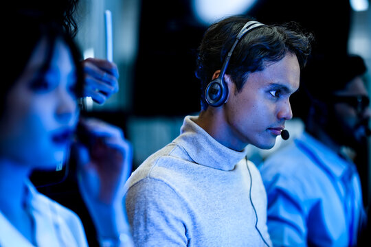 A diverse team of technical support specialists works a late shift in a busy call center. Focused operators with headsets assist clients, providing all day customer service.