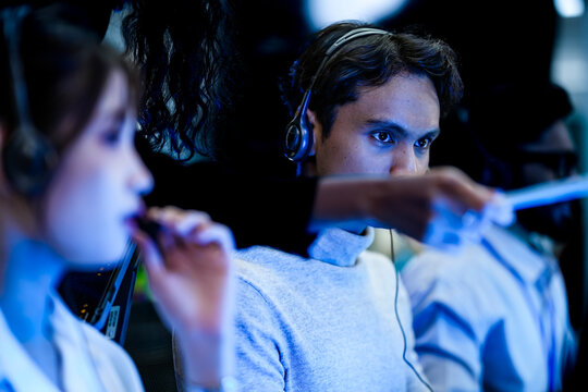 A diverse team of technical support specialists works a late shift in a busy call center. Focused operators with headsets assist clients, providing all day customer service.