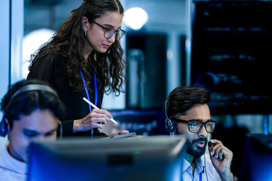 A diverse team of technical support specialists works a late shift in a busy call center. Focused operators with headsets assist clients, providing all day customer service.
