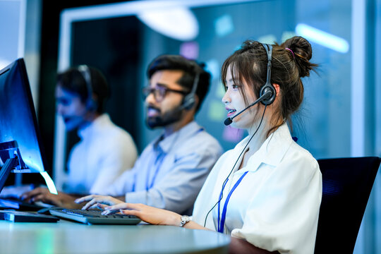 A diverse team of technical support specialists works a late shift in a busy call center. Focused operators with headsets assist clients, providing all day customer service.
