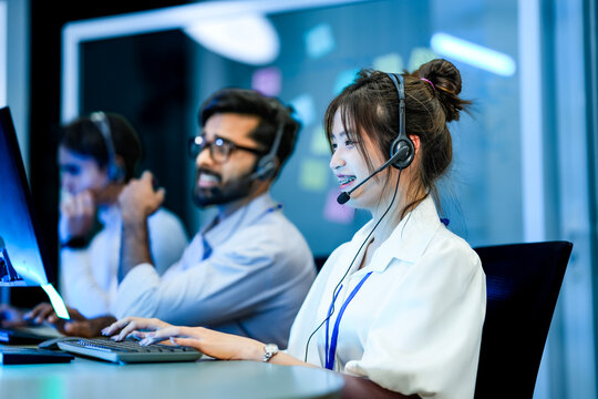 A diverse team of technical support specialists works a late shift in a busy call center. Focused operators with headsets assist clients, providing all day customer service.
