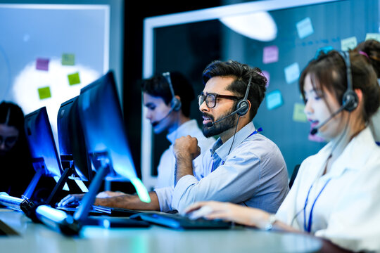 A diverse team of technical support specialists works a late shift in a busy call center. Focused operators with headsets assist clients, providing all day customer service.