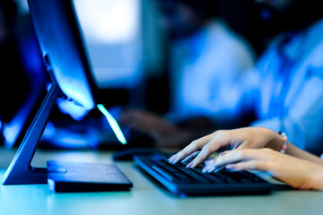 Close up of a customer service agent's hands typing on a backlit keyboard. A concept for data entry, online communication, and technical support in a modern call center office.