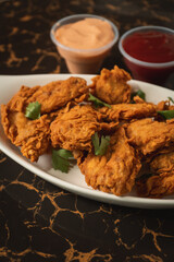 Close-up view of fried chicken with chopped vegetables on a plate surrounded by sauces.