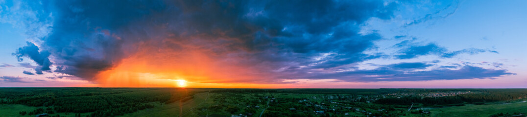 Dramatic stormy rain clouds over horizon at epic sunset. Aerial panorama.