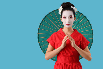 Beautiful young geisha with parasol on blue background