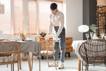 Young waiter pulling up chair at table in restaurant