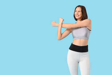 Sporty young woman stretching on blue background