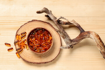 Composition with bowl of fish oil capsules and tree branch on wooden background