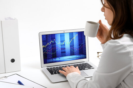 Female trader with coffee cup and laptop working at table in office, closeup