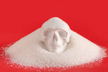 Heap of scattered sugar with human skull on red background