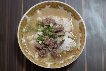 A close-up of a (coto makassar) delicious beef rice bowl with tender slices of beef, topped with...