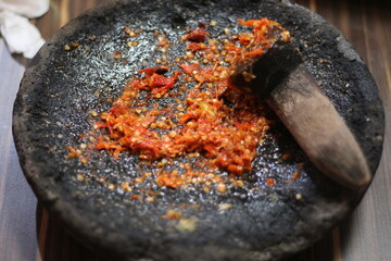 A close-up shot of freshly ground chili paste in a traditional stone mortar and pestle.