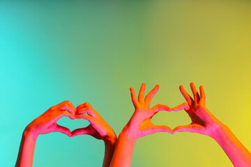 Toned female hands making heart gesture on color background
