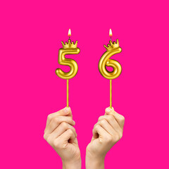 Birthday on a fuchsia background with the number 56 - Hands holding number-shaped candles