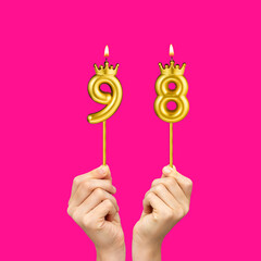 Birthday on a fuchsia background with the number 98 - Hands holding number-shaped candles