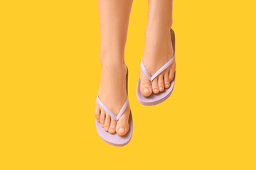 Legs of young woman in stylish lilac flip flops on yellow background