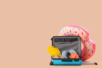 Suitcase, inflatable ring and beach accessories on beige background