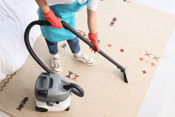 Male janitor with modern vacuum cleaner cleaning carpet in room
