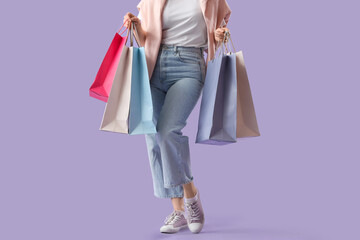 Beautiful young woman with shopping bags on purple background, closeup