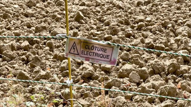 Close-up of a French cl&ocirc;ture &eacute;lectrique (electric fence) warning sign in a rural field