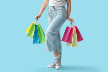 Beautiful young stylish woman with shopping bags on blue background, closeup
