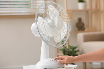 Female hand turning on electric fan in living room