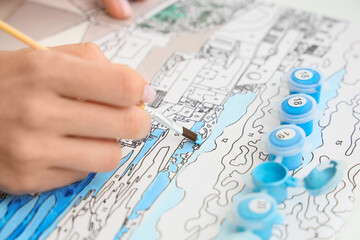 Female hand painting by numbers on canvas, closeup