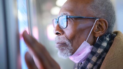 Elderly man wearing glasses and face mask looking thoughtfully digital screen public space with soft lighting and focused expression indoors scanning - Powered by Adobe