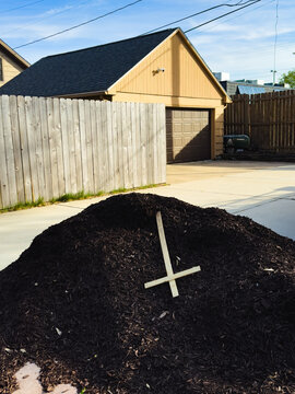 A pile of mulch with a cross on top in front of a house and wood fence
