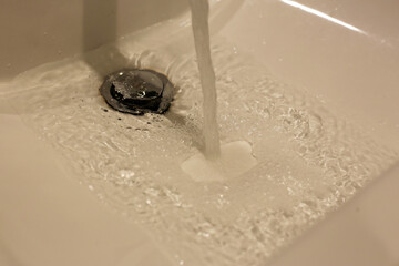 Running water from a stainless steel faucet into a white sink.