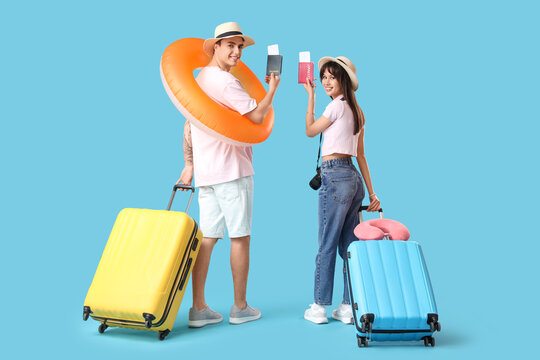 Couple of tourists with suitcases holding passports and swim ring on blue background, back view