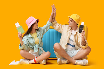 Couple of tourists with passports and suitcases giving each other high-five on yellow background