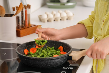 Woman with spoon frying vegetables on stove in kitchen, closeup