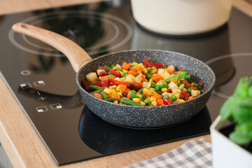 Frying pan with tasty vegetables on stove in kitchen, closeup