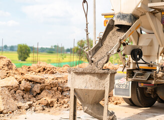 Fototapeta premium Concrete being poured from a cement mixer truck into a metal bucket at a construction site in a rural area.