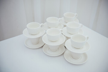 Lots of empty tea or coffee cups on a white table against a white wall, space for text.  Organization of events, catering, catering, beautiful white and gray background