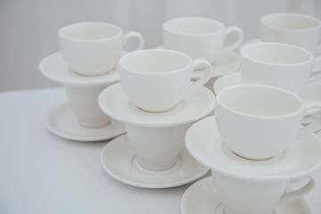 Lots of empty tea or coffee cups on a white table against a white wall, space for text.  Organization of events, catering, catering, beautiful white and gray background