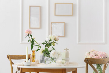Stylish table decorated with beautiful peonies and vases in dining room, closeup