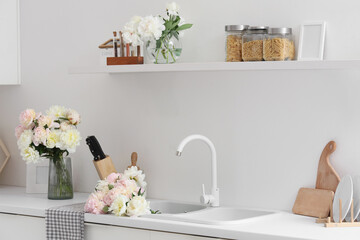 Interior of stylish kitchen with sink, shelf and beautiful peonies