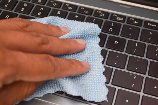 Hand cleaning laptop keyboard with blue microfiber cloth, concept of hygiene, device care, and electronic maintenance.