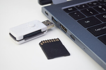 Close up USB card reader connected to laptop with microSD memory card, concept of data transfer, backup, and digital storage.