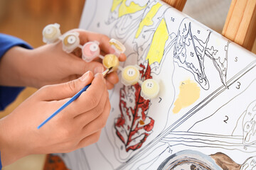 Female hands painting by numbers on easel in studio, closeup